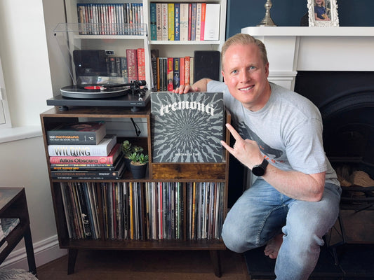 A man crouching next to a turntable and record storage unit, highlighting the album 'Marching in Time' by Tremonti.